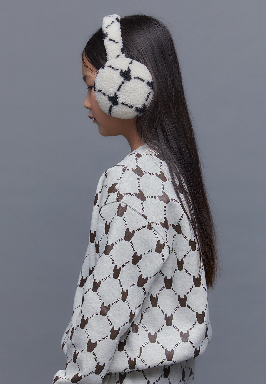 Woman wearing a patterned sweater and white fuzzy earmuffs against a gray background
