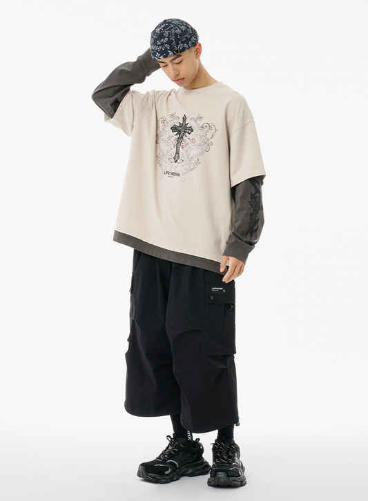 Person wearing a beige oversized shirt with a graphic design, black pants, and black shoes on a white background